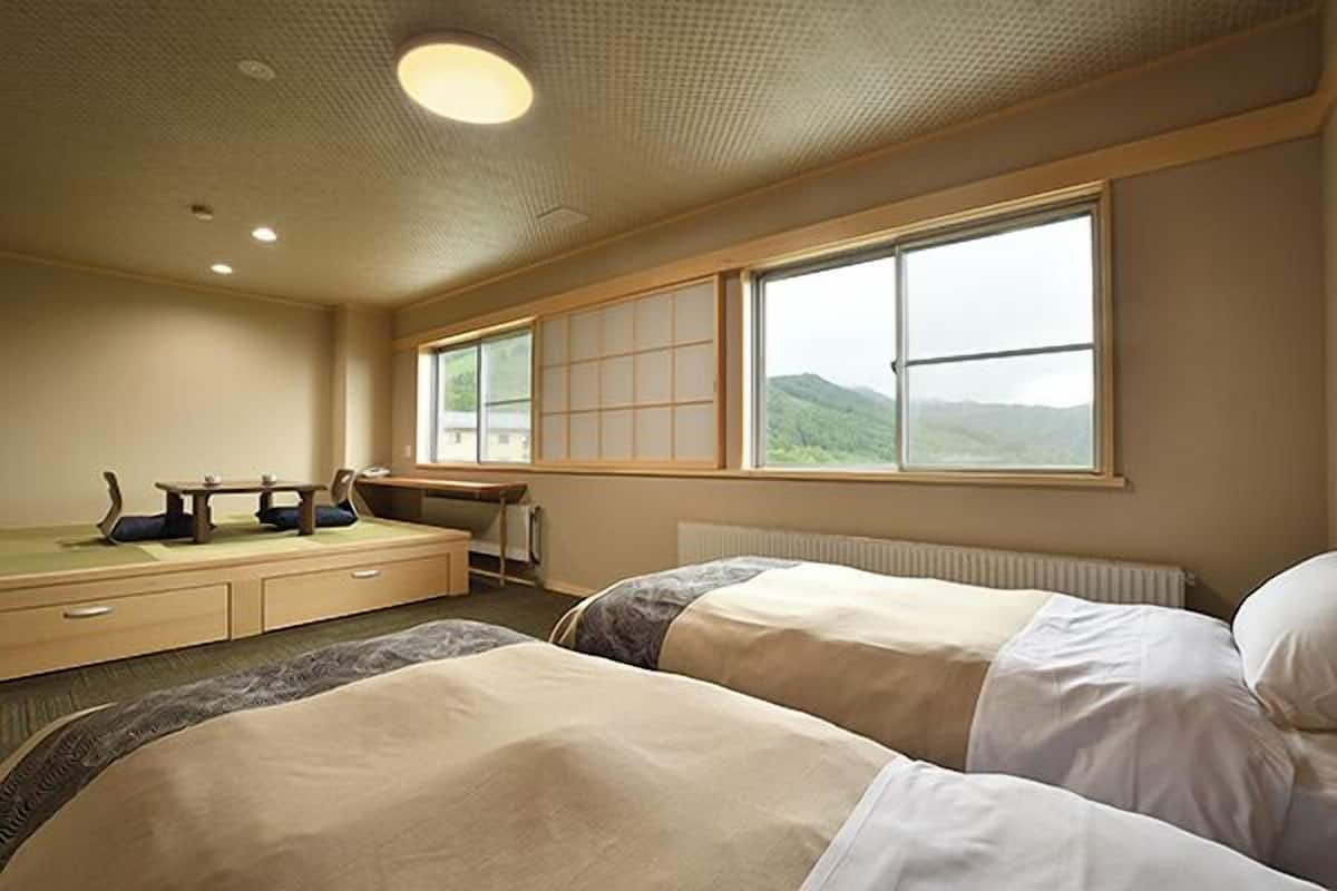 Une chambre d’hôtel avec deux lits, un bureau, une chaise et une grande fenêtre donnant sur des collines.