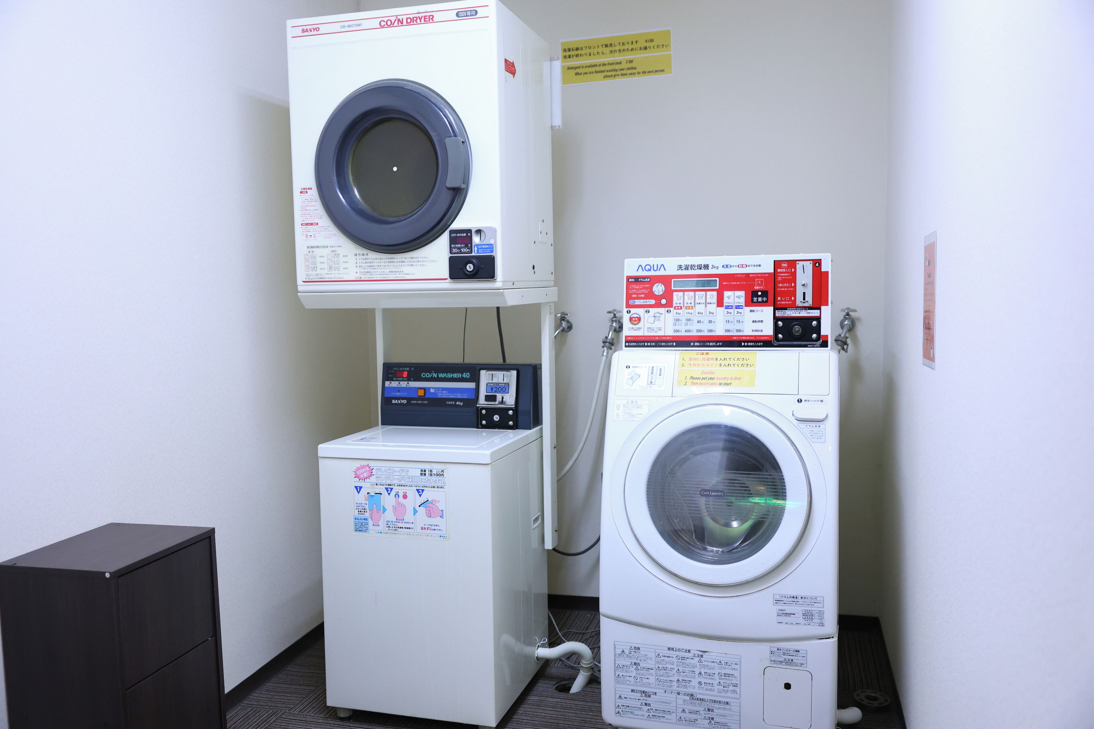 A laundry area with a front-loading washer and dryer, a small cabinet, and a sign on the wall.