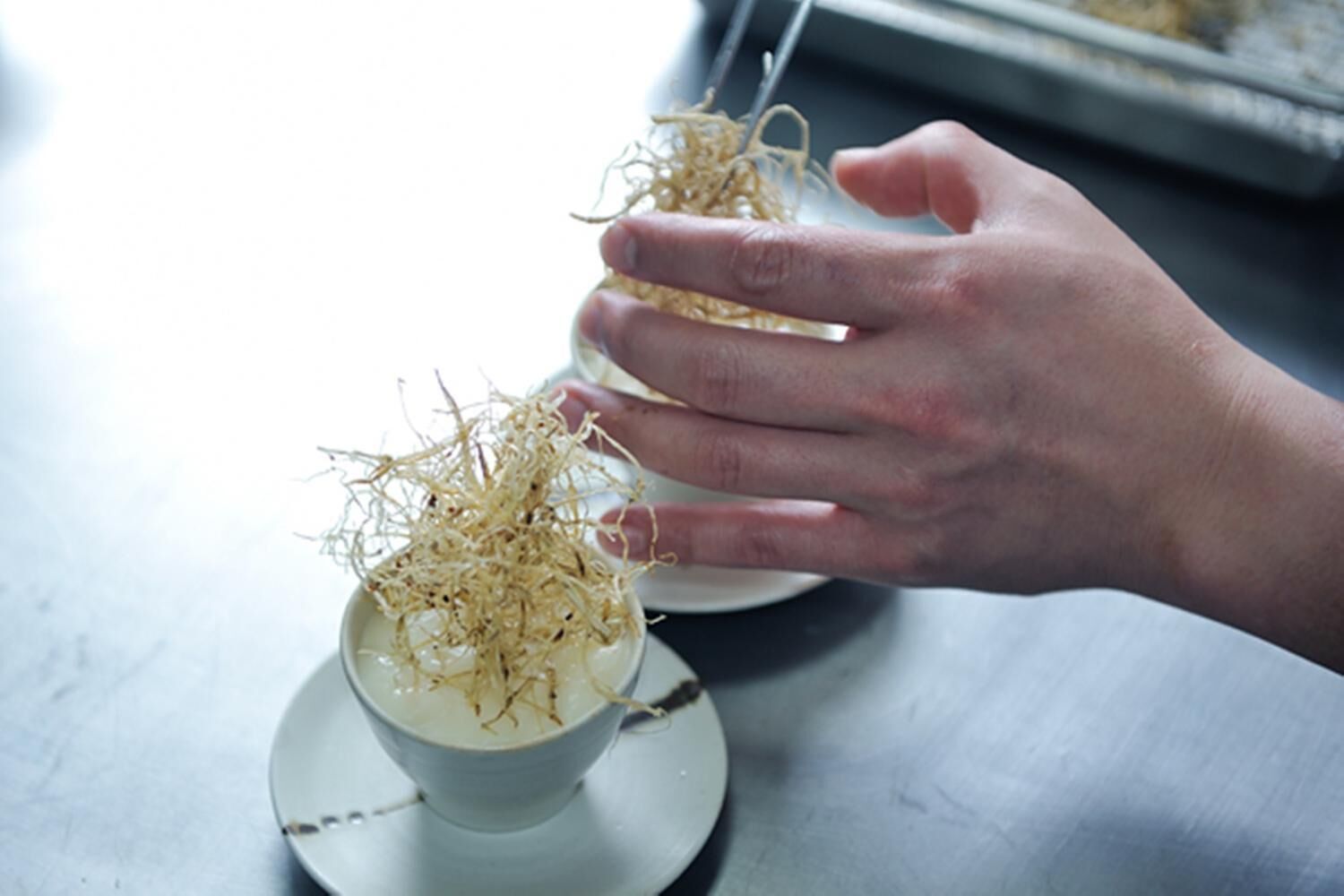 A hand holding a cup with a white substance and dried plant material.