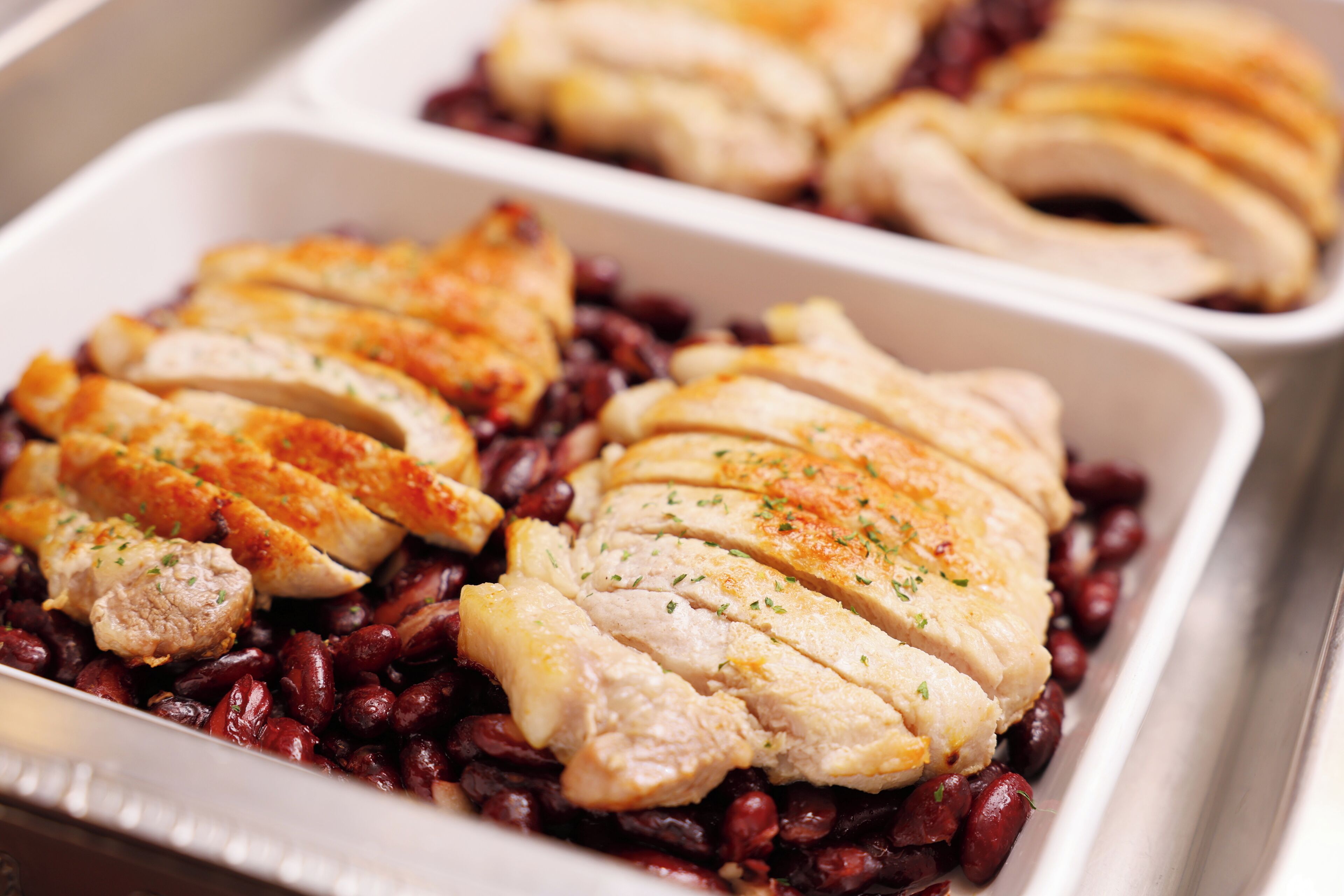 Una bandeja con pechugas de pollo en rodajas sobre frijoles rojos.