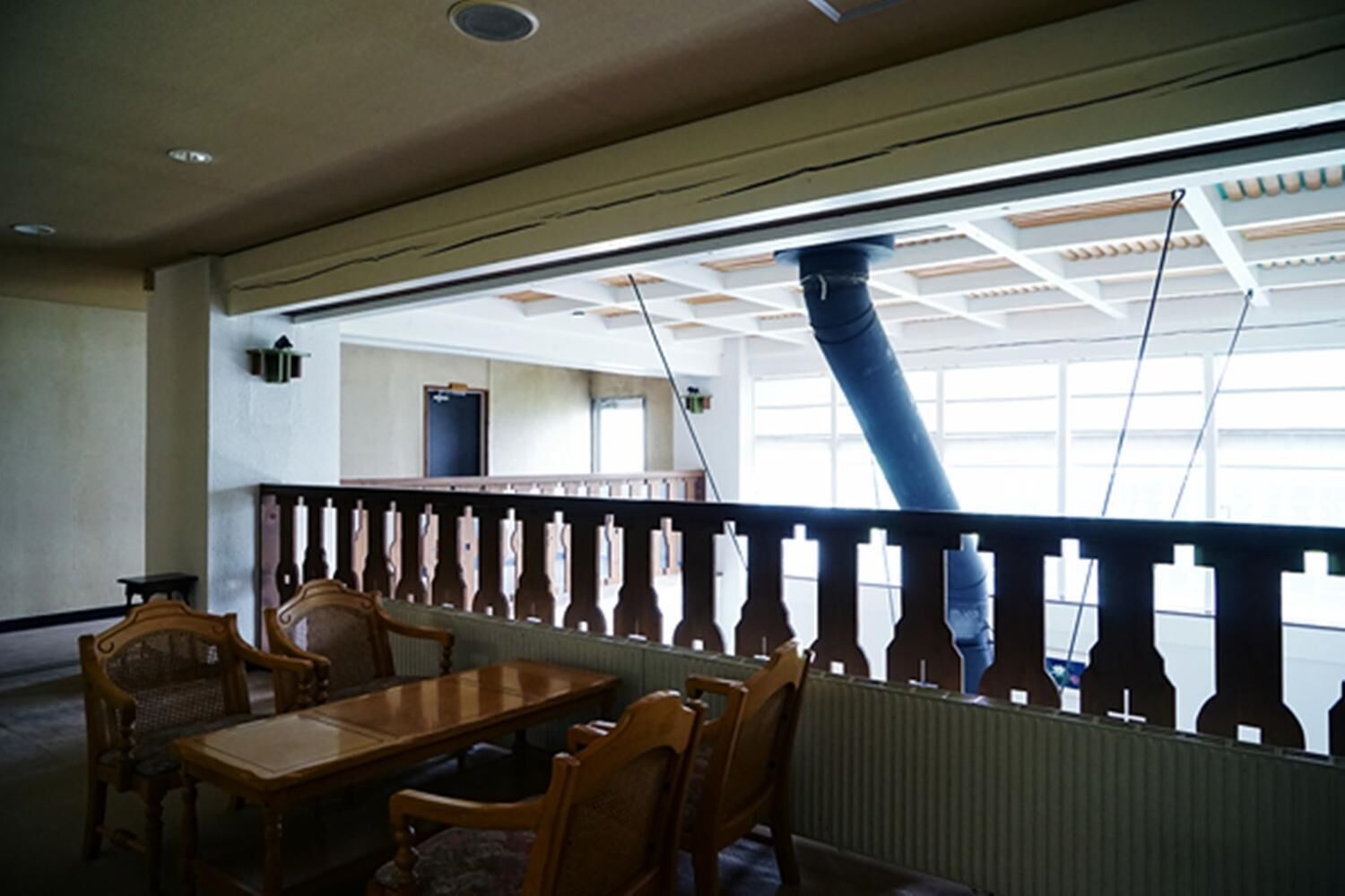 Ein Zimmer mit einem Holztisch und Stühlen, einem Fenster mit Blick auf ein Gebäude und einer Decke mit einem Oberlicht.
