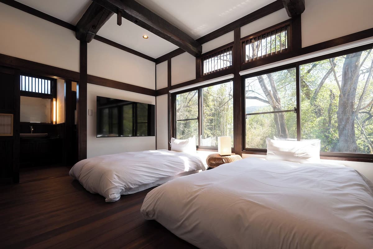 A bedroom with two beds, a large window, and a wooden ceiling.