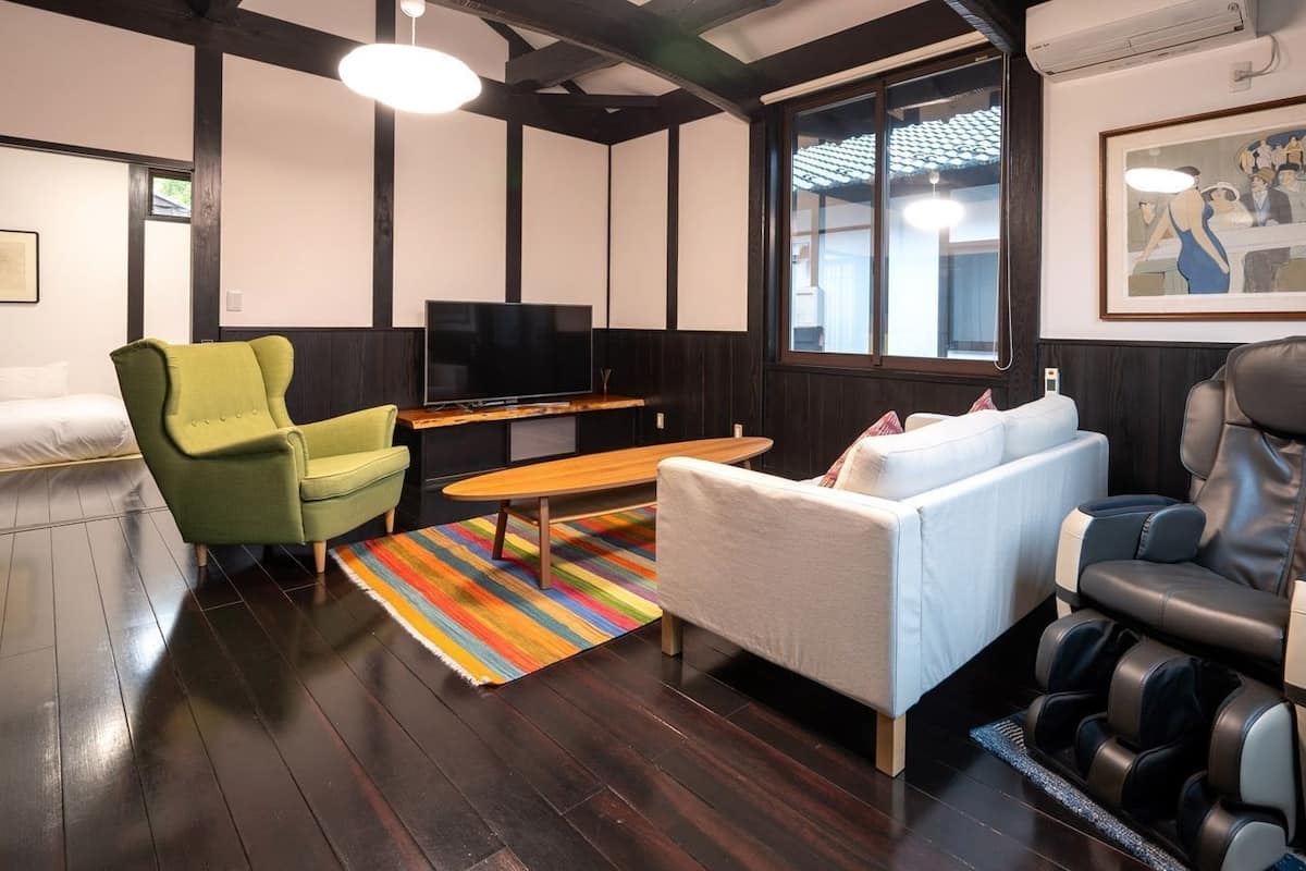A modern living room with a sofa, armchair, massage chair, TV, and a colorful striped rug.