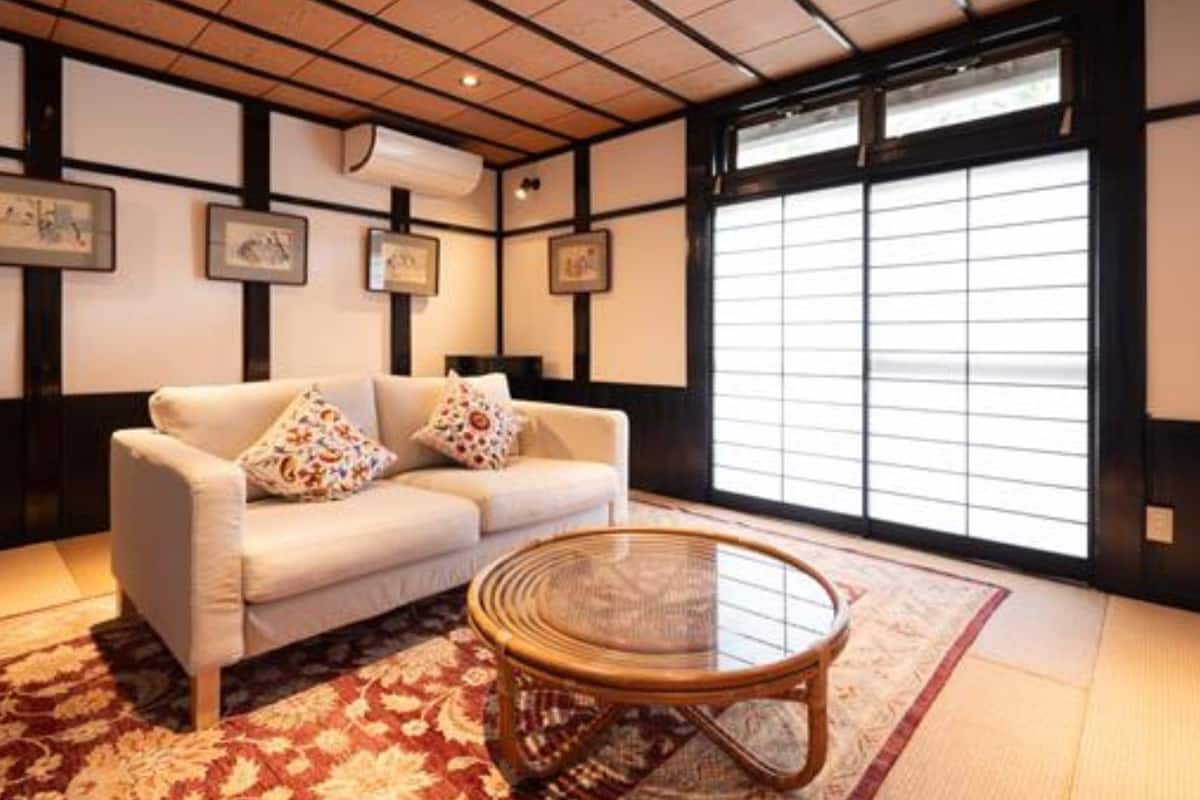 Perinteinen japanilaistyylinen huone, jossa on tatamimatto, matala puupöytä, tyynyillä varustettu sohva ja liukuvat shoji-seinäpaneelit.