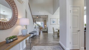 A spacious hallway with a wooden bench, a round mirror, and a lamp. A staircase with a wooden railing leads to another room. - Lovely 5 bedroom pool and spa home with fantastic cinema in Windsor Hills Resort (Kissimmee)