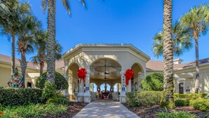 A hotel entrance with a covered walkway, palm trees, and red bows on columns. - Lovely 5 bedroom pool and spa home with fantastic cinema in Windsor Hills Resort (Kissimmee)