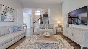 A spacious living room with a sofa, coffee table, and TV. A staircase leads to another room. - Lovely 5 bedroom pool and spa home with fantastic cinema in Windsor Hills Resort (Kissimmee)