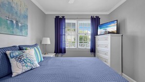 Een slaapkamer met een groot bed, een dressoir, een televisie en een raam met gordijnen.