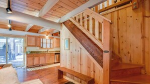 Amplia sala de estar con una escalera de madera, una cocina con armarios de madera y un gran ventanal que proporciona luz natural.