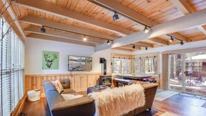 Una sala de estar acogedora con techo de madera, un sofá, chimenea y un ventanal con vistas a una terraza.