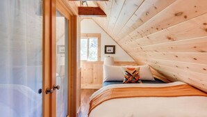 Un dormitorio con techo inclinado de madera, una cama con un cojín de colores y una ventana con vistas al exterior.