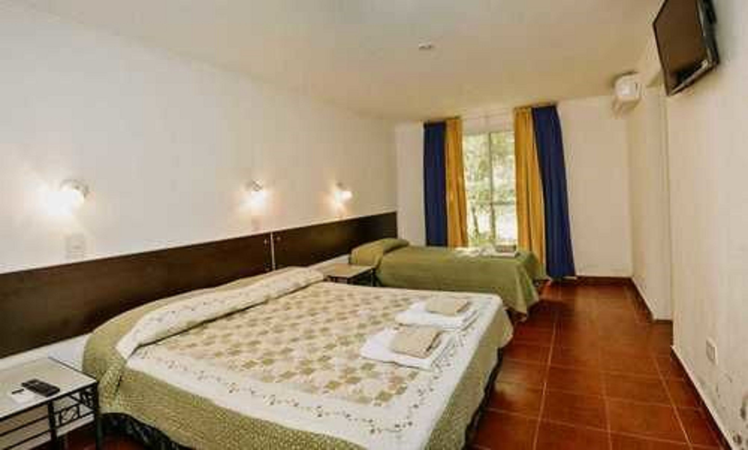 A hotel room with two beds, a television mounted on the wall, and a window with curtains.