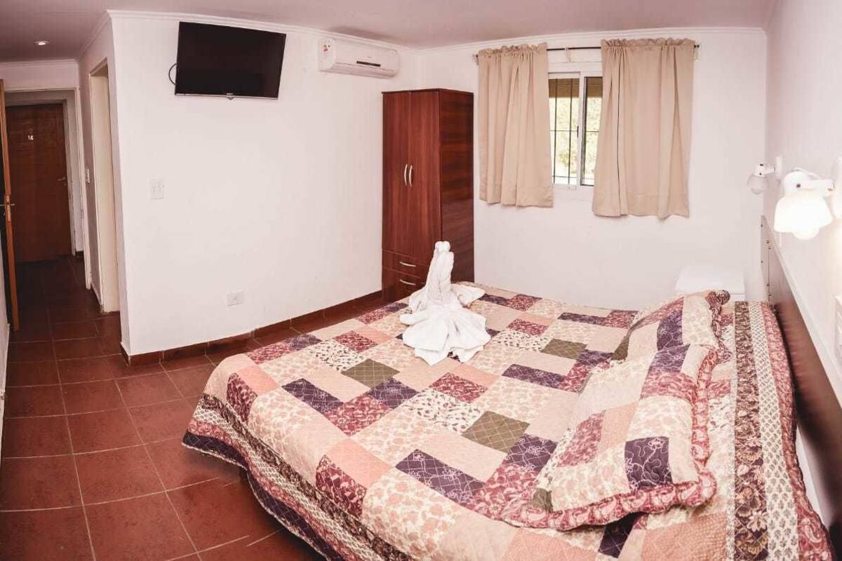 Een slaapkamer met een groot bed, een kledingkast, een televisie aan de muur en een raam met gordijnen.
