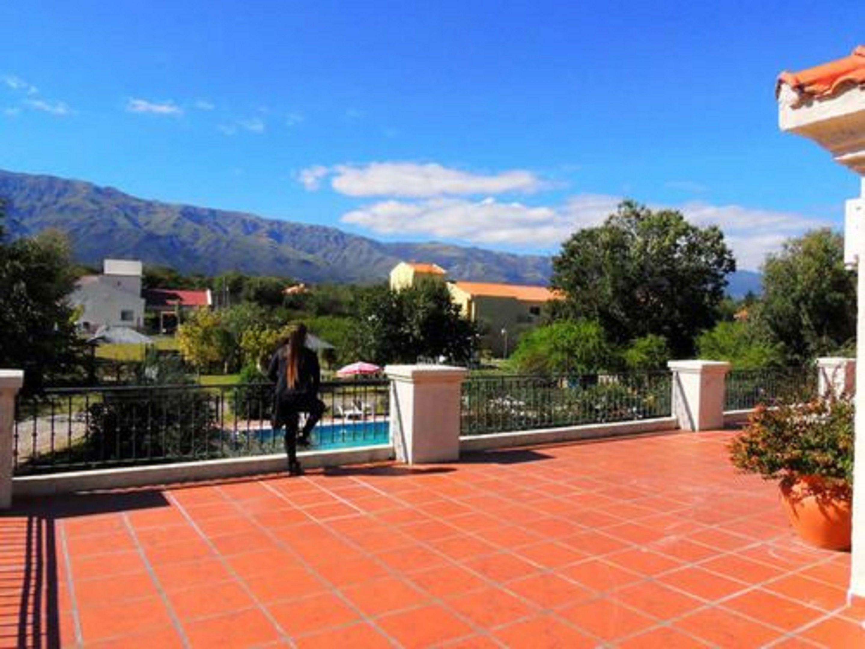 A terrace with red tiles, a white column, and a view of mountains and houses.
