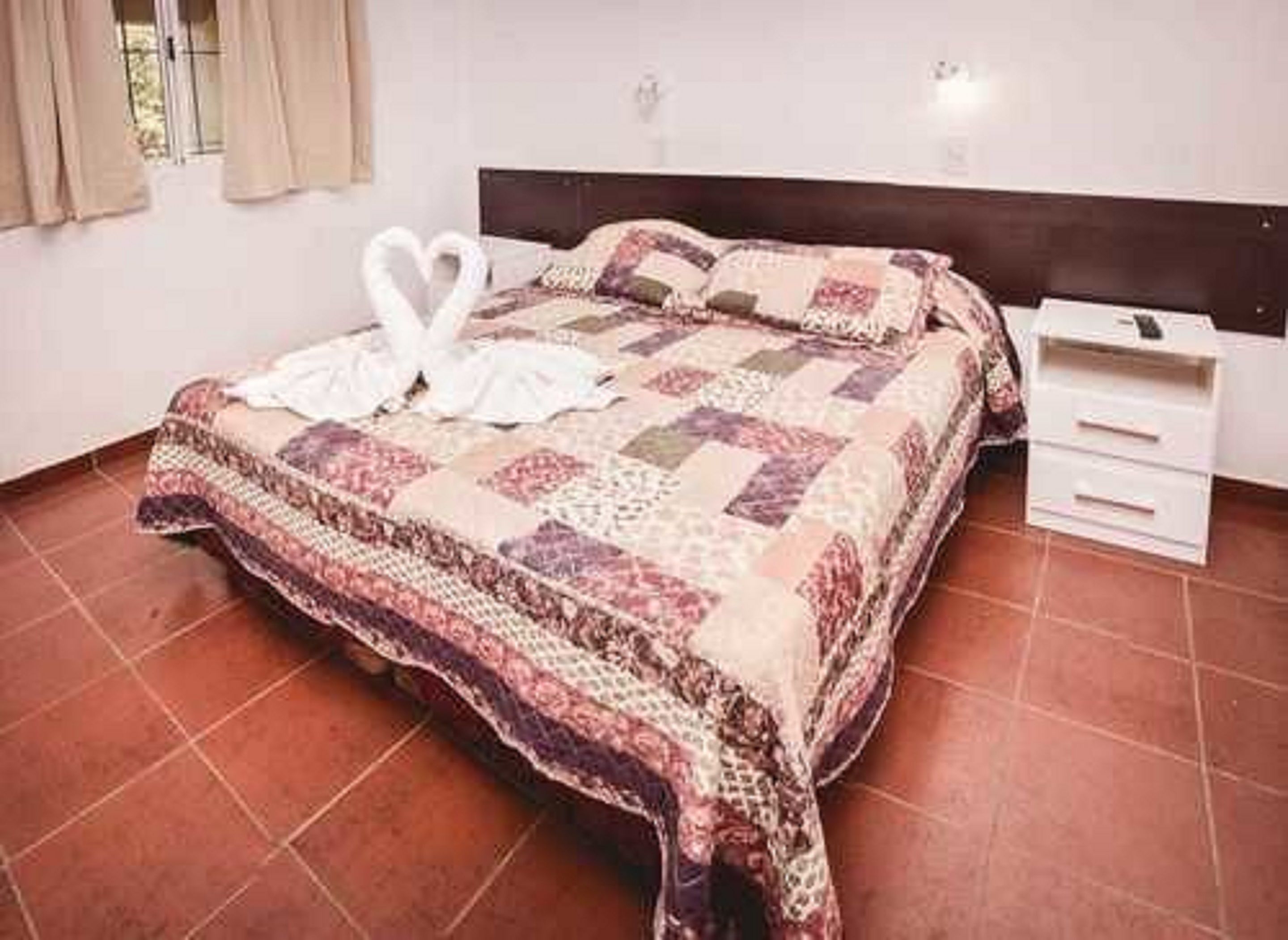 Una cama bien hecha con una colcha estampada y dos toallas blancas dispuestas en forma de corazón.