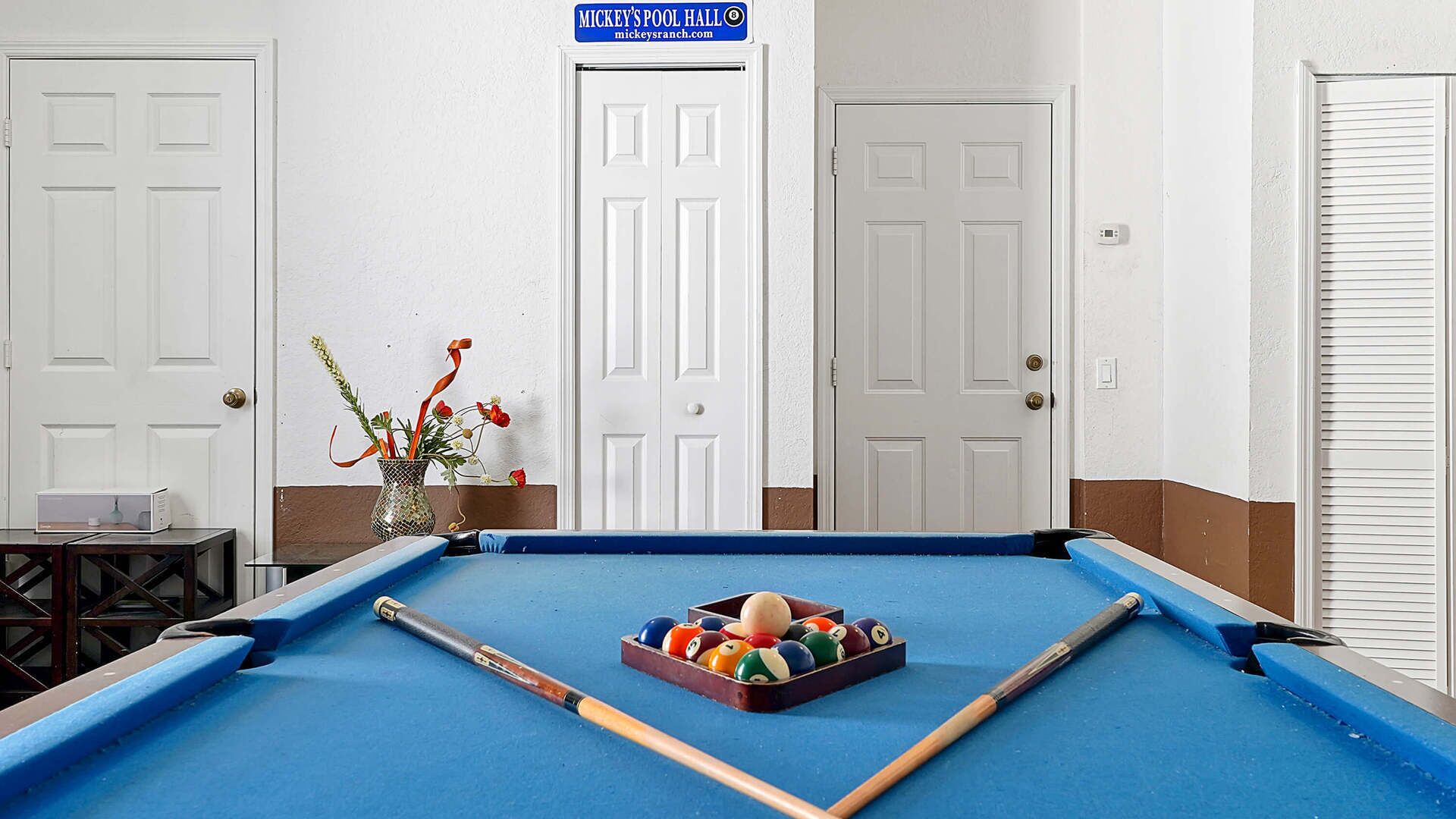 A pool table with balls and cues, a vase with flowers, and a sign above a door.