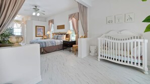 Une chambre à coucher avec un lit, un berceau, une table de chevet, une lampe et un ventilateur de plafond.