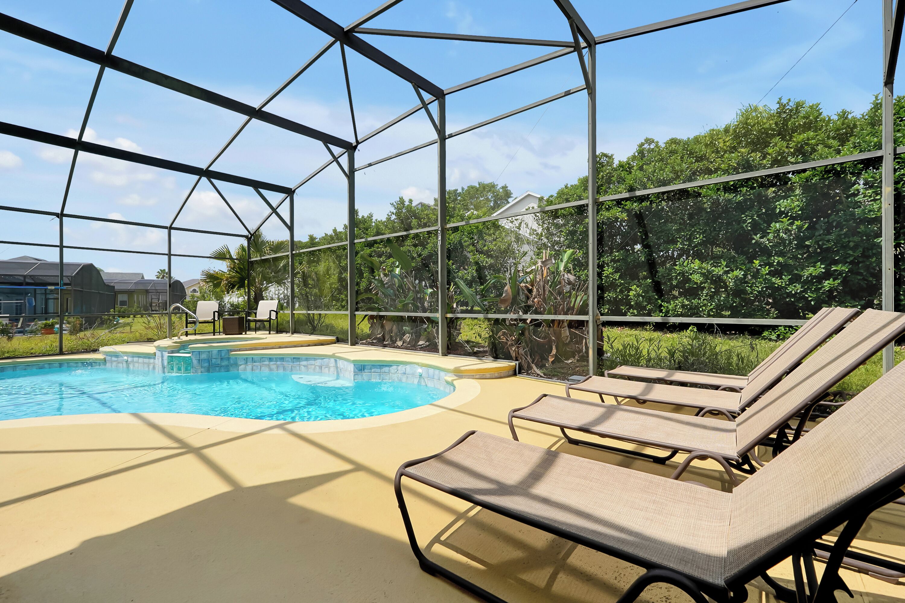 A pool area with a clear blue pool, surrounded by a metal enclosure, and includes lounge chairs and a view of greenery.