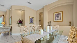 Une salle à manger avec une table en verre, des chaises décorées et des œuvres d’art encadrées accrochées aux murs.