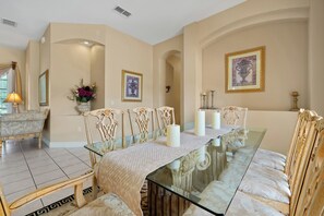 A dining room with a glass table, ornate chairs, and framed artwork on the walls. - Dazzling Disney Getaway - Closest to Disney  Villa with Private Pool & Game Room (Kissimmee)