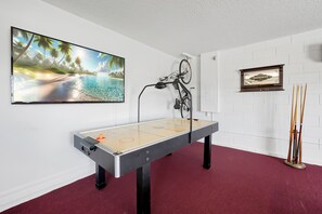 A room with a foosball table, a mounted bicycle, a framed picture, and a large beach scene painting on the wall. - Dazzling Disney Getaway - Closest to Disney  Villa with Private Pool & Game Room (Kissimmee)