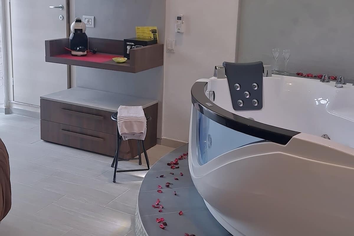 Une salle de bain avec une baignoire, un lavabo et des toilettes. On y trouve une étagère avec des articles de toilette et un tableau encadré au mur.