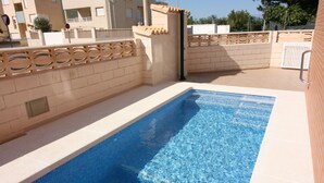 A rectangular swimming pool with clear blue water, surrounded by beige tiled walls and a decorative wooden fence. - OLIVA HOLIDAYS 2- BY THE SEA WITH SWIMMING POOL (Oliva)