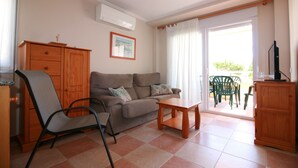 A living room with a sofa, a chair, a small table, a cabinet, and a television. - OLIVA HOLIDAYS 2- BY THE SEA WITH SWIMMING POOL (Oliva)