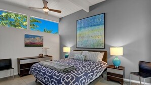 Une chambre à coucher moderne avec un grand lit, deux tables de chevet, un ventilateur de plafond et des œuvres d’art accrochées aux murs.