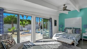 Une chambre avec un lit, un ventilateur de plafond et une vue sur l’extérieur grâce à de grandes portes-fenêtres coulissantes.