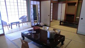 Una habitación japonesa tradicional con suelo de tatami, una mesa baja con cojines, una puerta corredera y vistas a un jardín.