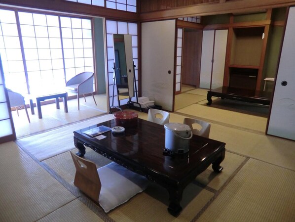A traditional Japanese room with tatami flooring, a low table with cushions, a sliding door, and a view of a garden. - Leo Plaza Hotel Sasebo (Sasebo)