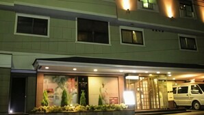 Un hotel de varios pisos con una entrada bien iluminada, una zona de estacionamiento y un vehículo visible.
