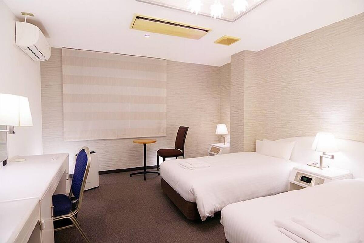 Habitación de hotel con dos camas, un escritorio, una silla, una mesita y un aire acondicionado de pared.