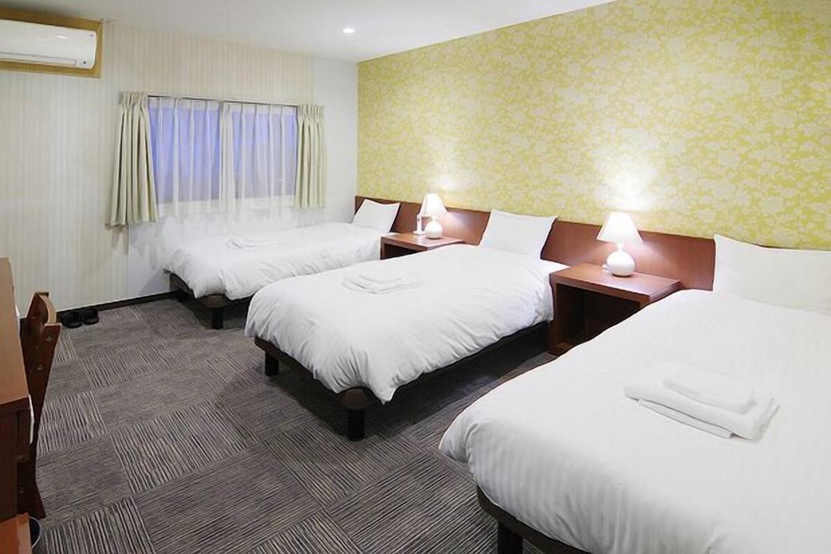Habitación de hotel con tres camas, un escritorio y una ventana con cortinas.