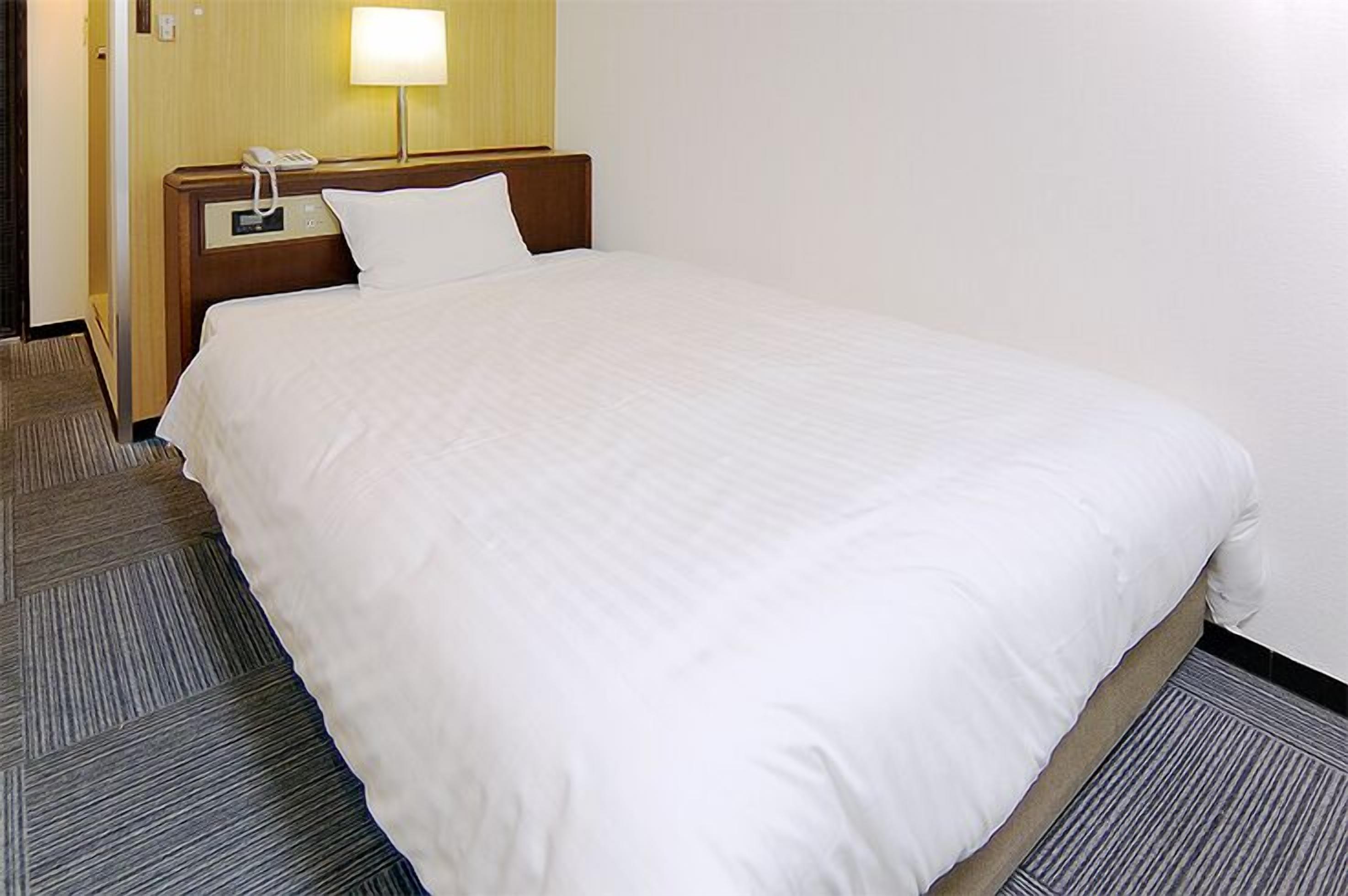 Una habitación de hotel con una cama grande, un teléfono en la mesita de noche y una lámpara.