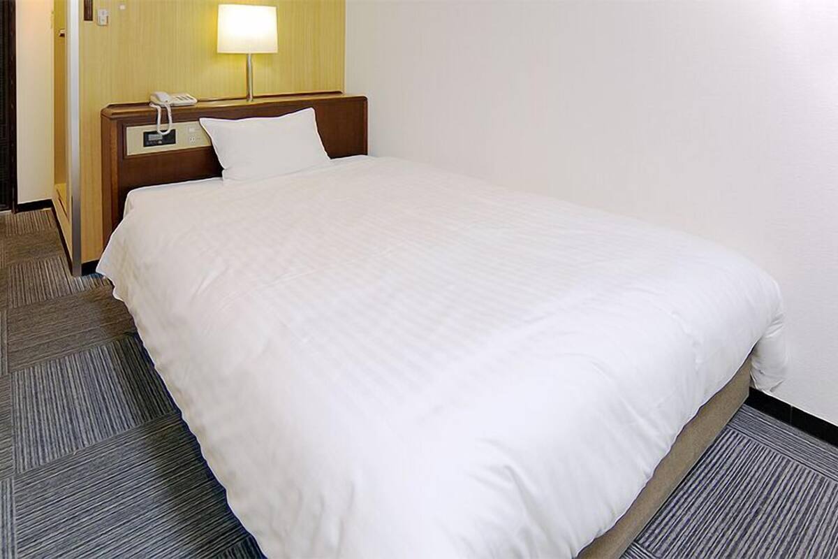 Una habitación de hotel con una cama grande, un teléfono en la mesita de noche y una lámpara.