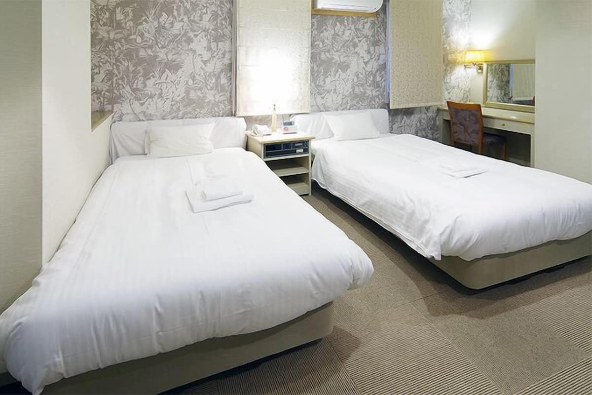 A hotel room with two beds, a nightstand, a mirror, and a window with a view.