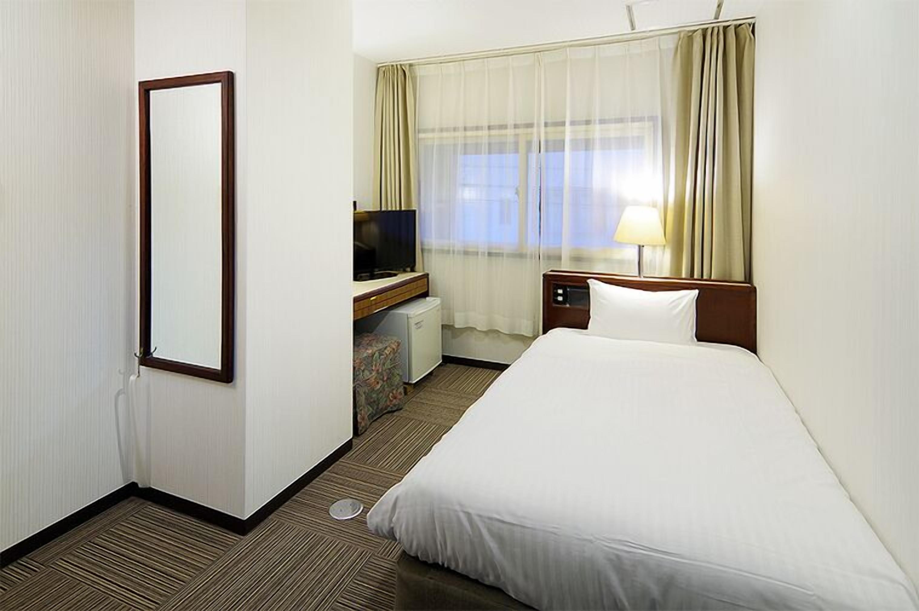 Una habitación de hotel con cama, televisión, escritorio, lámpara y ventana con cortinas.