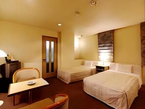 Habitación de hotel con dos camas, un escritorio, una silla, una lámpara de escritorio y un televisor montado en la pared.