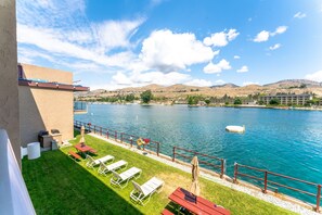 A lakeside patio with lounge chairs, a barbecue area, and a view of the lake and hills. - Grandview 623 Waterfront condo on Lake Chelan (Chelan)