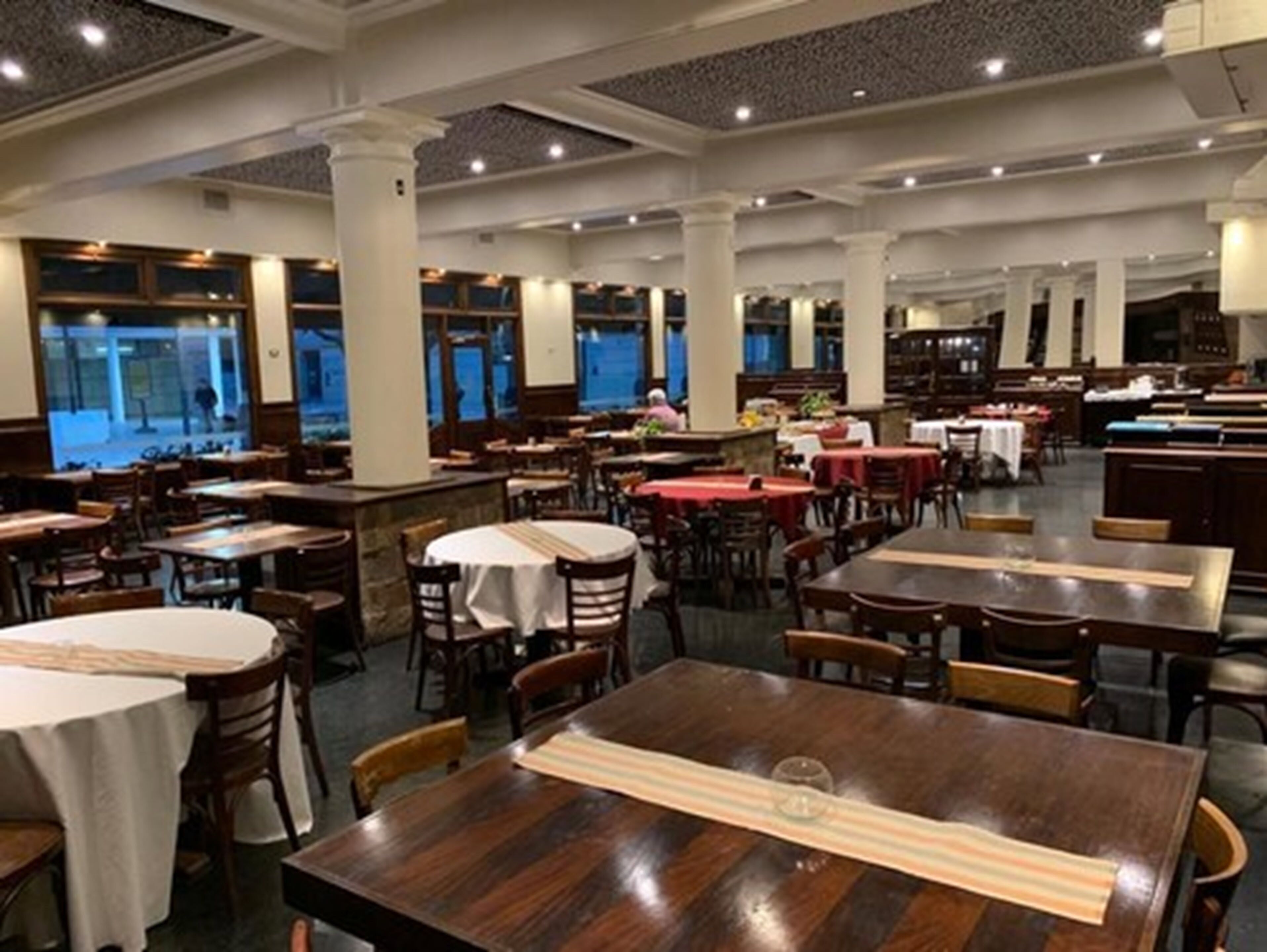 A spacious restaurant with multiple tables and chairs, large windows, and a high ceiling.