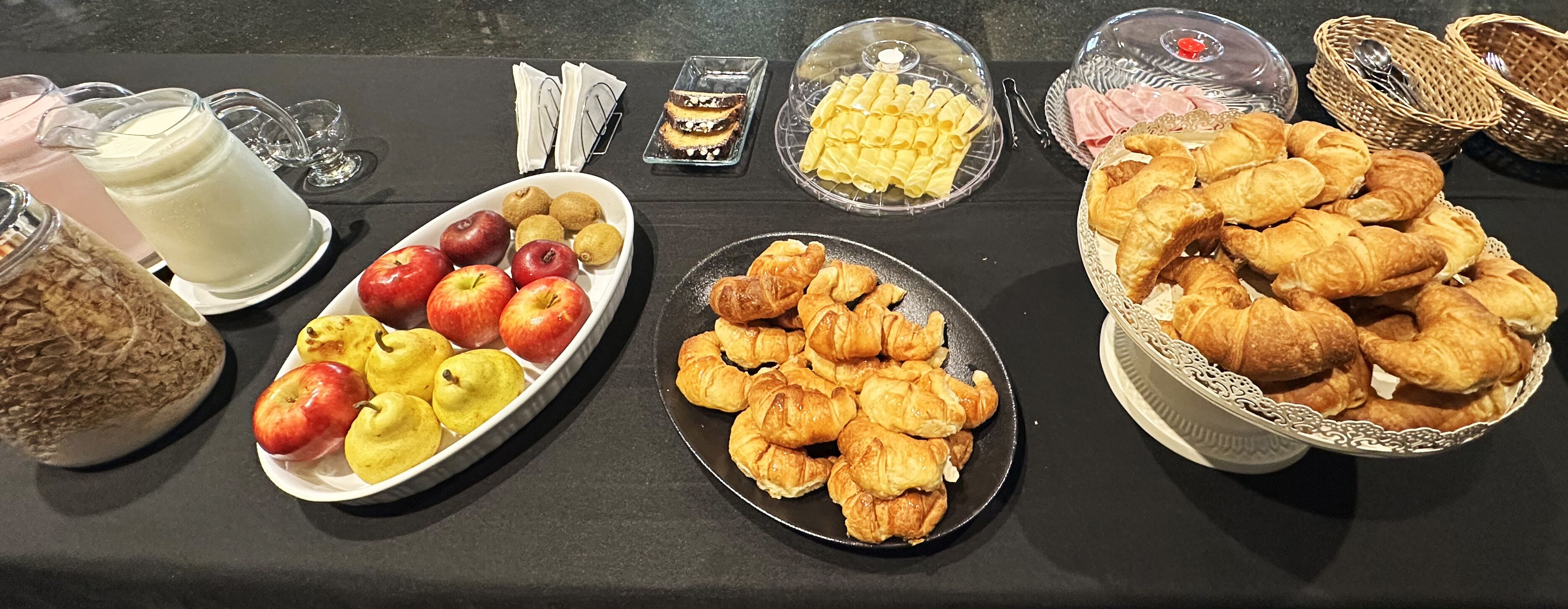 A buffet table with various food items including apples, pears, pastries, and a milk pitcher.