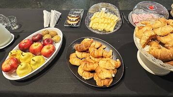 A buffet table with various food items including apples, pears, pastries, and a milk pitcher.