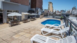 Área de piscina en la azotea con sillones de descanso, sombrillas y vistas de la ciudad.