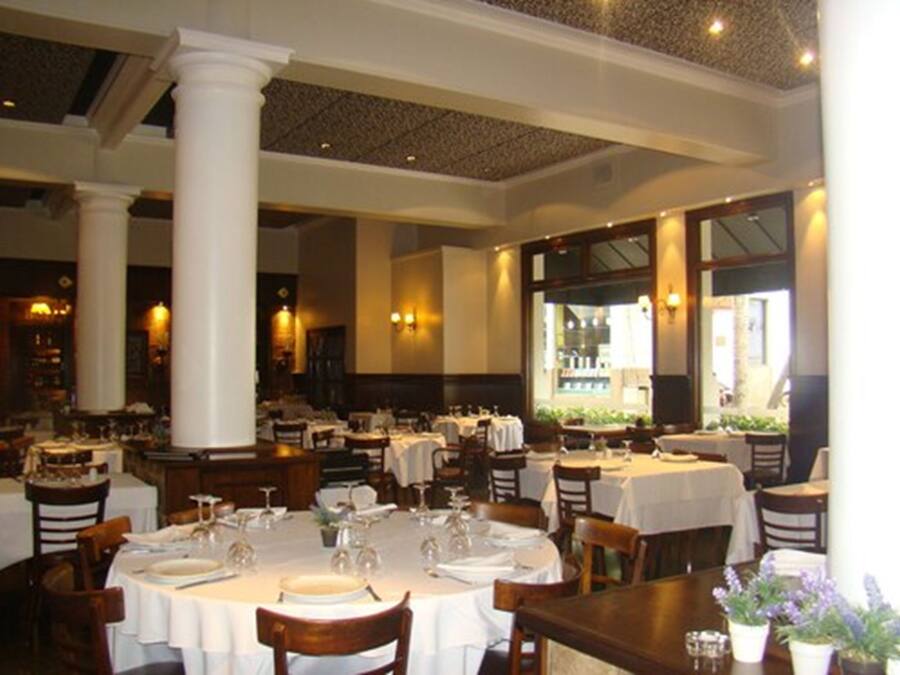 A restaurant with round tables, white tablecloths, and wooden chairs.