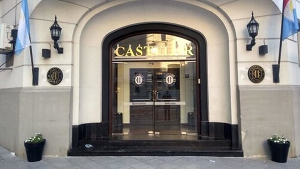 Entrada de hotel con un amplio arco de entrada, dos banderas a cada lado y un cartel sobre la puerta.