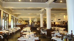 Un restaurante espacioso con mesas largas, columnas blancas y un techo alto.