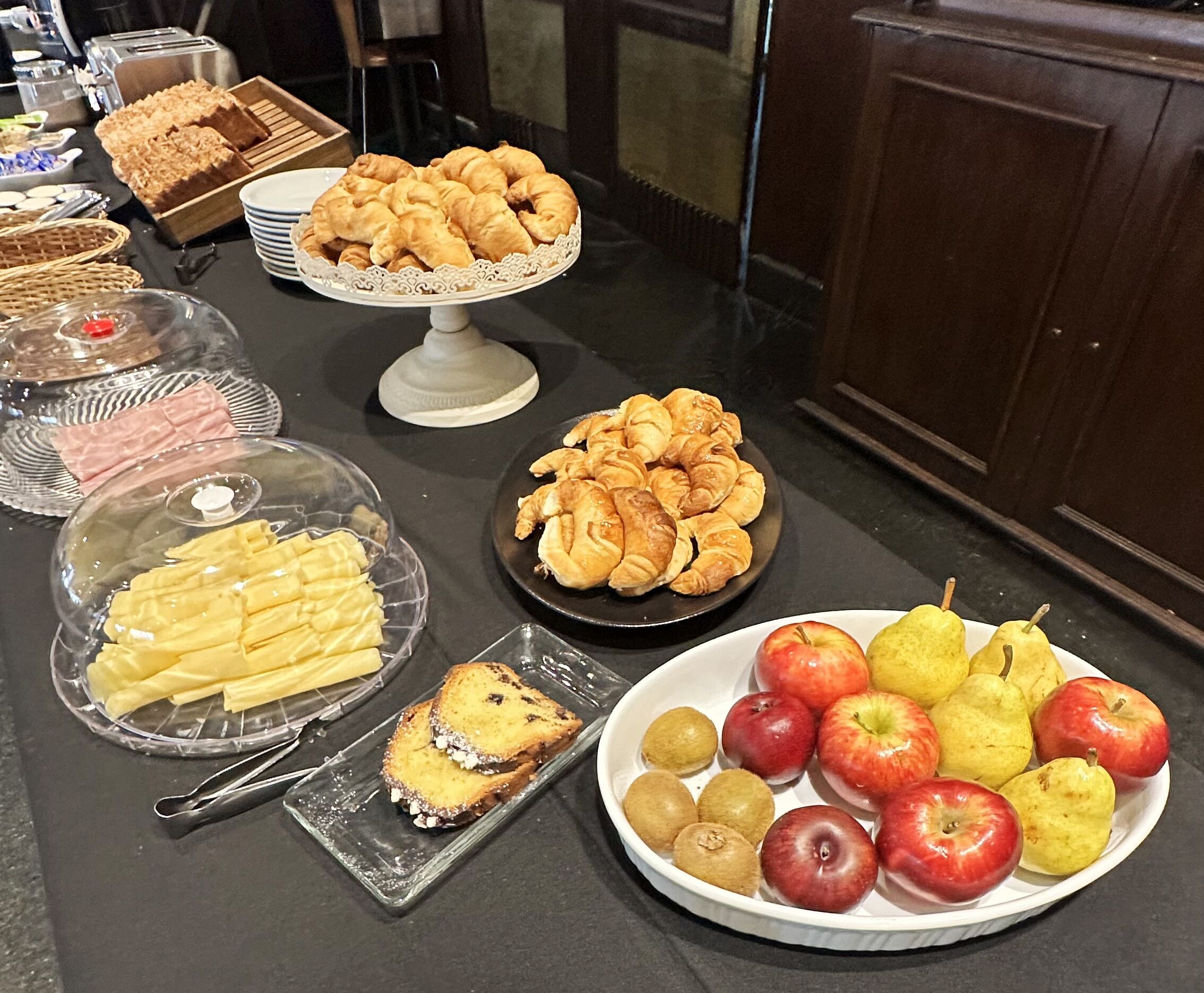 Une table de buffet proposant divers aliments, notamment des croissants, des fruits et des pâtisseries.