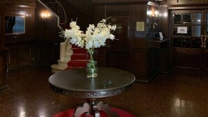 Un vestíbulo con una imponente escalera, un candelabro y una mesa redonda con un jarrón de flores.